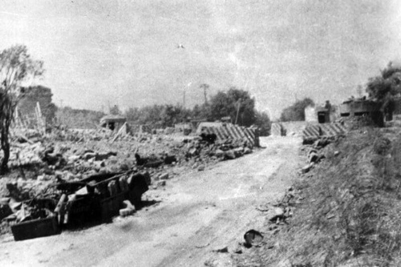 This view of Bivio Jazzotto, looking south from the Primosole Bridge, captures a significant moment from the aftermath of the battle. In the foreground, the presence of a Sahariana—a specialized Italian reconnaissance vehicle—serves as evidence of the fierce counterattacks launched by the Italian "Arditi" units.