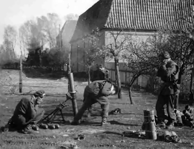 A 2 Special Air Service mortar section fires round after round into a stubborn pocket of German resistance, their 3-inch mortar thumping steadily as smoke and shrapnel tear into enemy positions. The ground shakes with each detonation as the SAS gunners adjust their range, relaying fire missions from forward jeep patrols operating just ahead.