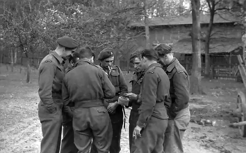 A group of 1 Special Air Service soldiers stand together somewhere in Germany, sharing a cigarette in a rare moment of calm. Their uniforms are dusty, their faces drawn with the fatigue of weeks spent on continuous operations behind enemy lines.