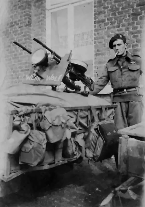 An SAS trooper stands proudly beside his jeep-mounted twin Vickers K machine guns, a hallmark of the regiment’s fast and heavily armed reconnaissance vehicles. Between the two barrels sits a mounted searchlight, a field modification occasionally used during night operations or in the final phases of the European campaign when mobility and visibility were crucial.
Painted beneath the gun mount is the name “Wehr Wolf”—likely a grim play on the German word Werwolf, referencing both the Nazi guerrilla resistance movement and the feral symbolism embraced by many SAS patrols.