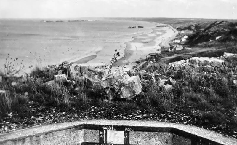 Photo shows Tobruk Mortar opening with painted terrain for target reference, and two Widerstandnest 72 casemates visible below on the beach.