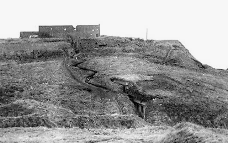 Photo clearly shows zigzag trenches, two dugouts, and the ruins of Maison Gambier visible in the background.