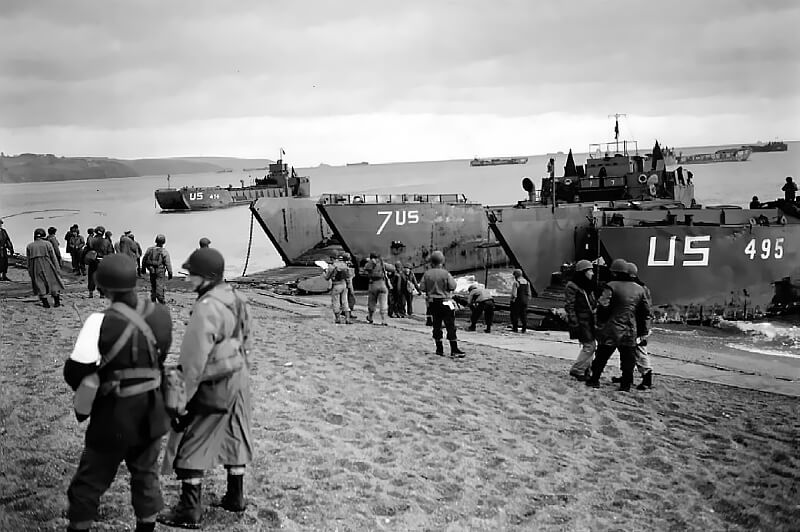 American LCTs beached on the shingle at Slapton Sands; foreground officer with white armband serves as exercise umpire.