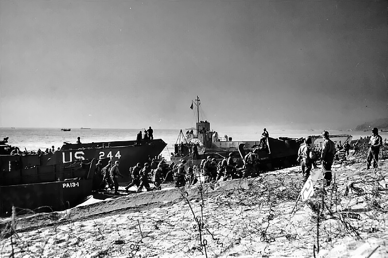 U.S. Troops coming ashore during an exercise, with an M7 105 mm self-propelled howitzer visible on the beach.