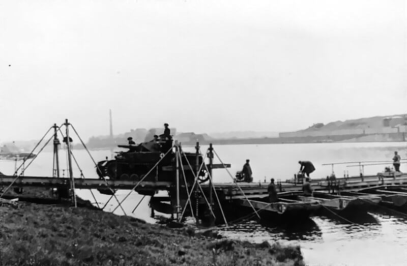 May 1940. German troops conduct a river crossing over the Maas during the Western Campaign, moving men and equipment across the water in an organised operation as the advance pushes deeper into the Netherlands and Belgium.