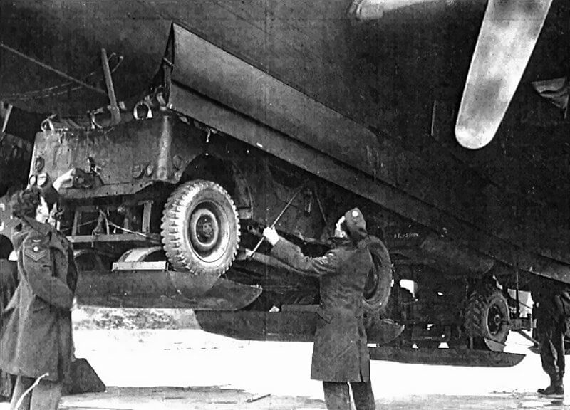 The jeep is suspended beneath the aircraft’s fuselage, with the bomb aimer operating the release mechanism used for supply containers.